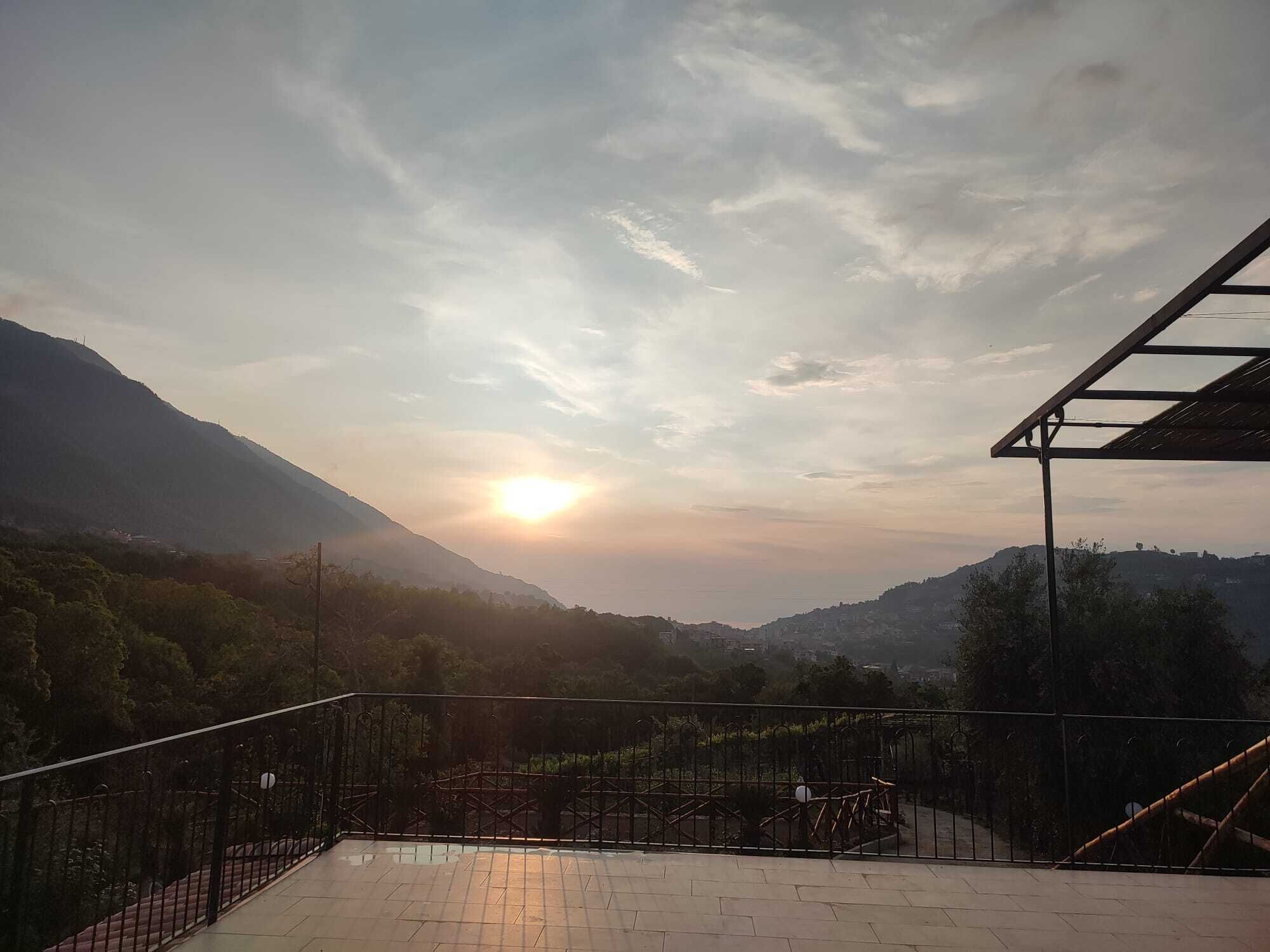 A terrace with a view of a mountainous landscape and the sun setting in the distance.