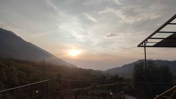 A terrace with a view of a mountainous landscape and the sun setting in the distance.