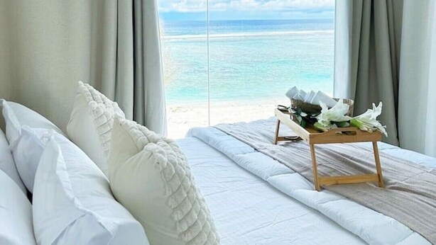 A bedroom with a large bed, white bedding, and a view of the ocean. - Lazzlla 1BR beachfront oceanview apartment (Hulhumale city Kaafu)