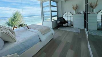 A bedroom with a large bed, a desk, and a view of the ocean.