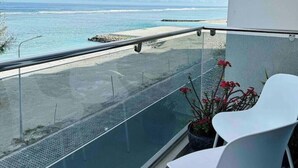 A balcony with a glass railing overlooking a beach. - Lazzlla 1BR beachfront oceanview apartment (Hulhumale city Kaafu)
