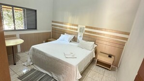 A hotel room with a bed, bedside table, and a window with blinds. - Pousada Portal do Manso (Cuiabá)