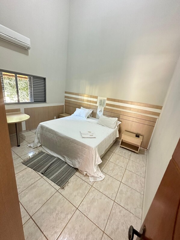 A hotel room with a bed, bedside table, and a window with blinds. - Pousada Portal do Manso (Cuiabá)