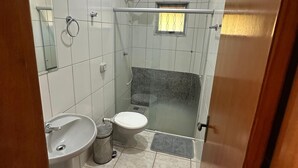 A bathroom with white tiles, a sink, a toilet, a shower with a glass door, and a small window. - Pousada Portal do Manso (Cuiabá)