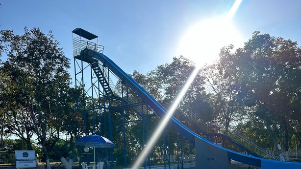A swimming pool with a blue slide, surrounded by trees and a clear sky. - Pousada Portal do Manso (Cuiabá)