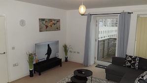 A modern living room with a flat-screen TV, a sofa, a coffee table, and a decorative globe. - Charming 1-bed Apartment in Barking (Barking)