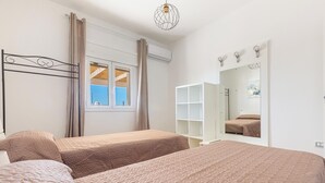 A bedroom with two beds, a window with curtains, an air conditioning unit, a mirror, and a white wardrobe. - 3863 Dimora Le Frasche - Trilo 1 by Barbarhouse (Porto Cesareo)