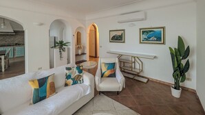 A modern living room with a white sofa, a dining table, and a large potted plant. - Perfect destination for families and friends, nestled between seas and mountains (Praiano)