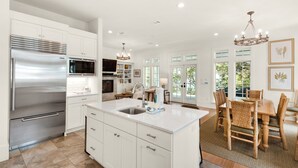 A modern kitchen with a large island, stainless steel appliances, and a dining area with wooden furniture. - SOUTH OF 30A~Walk to beach~4 Bikes!POOL! Sleeps 10 (Santa Rosa Beach)