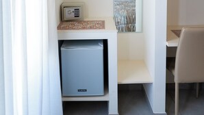 A compact room with a bed, a small desk, a chair, a mirror, a safe, and a shelf with a magazine rack. - Le2Stanze  (Vittoria)