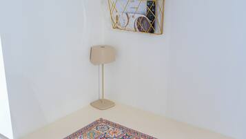 Un escritorio blanco con un mantel decorado, una lámpara y un organizador de pared con papeles y un teléfono.