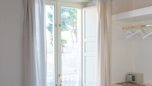 A bedroom with a bed, a small desk with a radio, and a window with curtains. - Le2Stanze  (Vittoria)