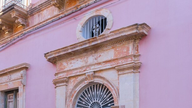 A building with a black door, a small window with a metal grille, and a stone base. - Le2Stanze  (Vittoria)