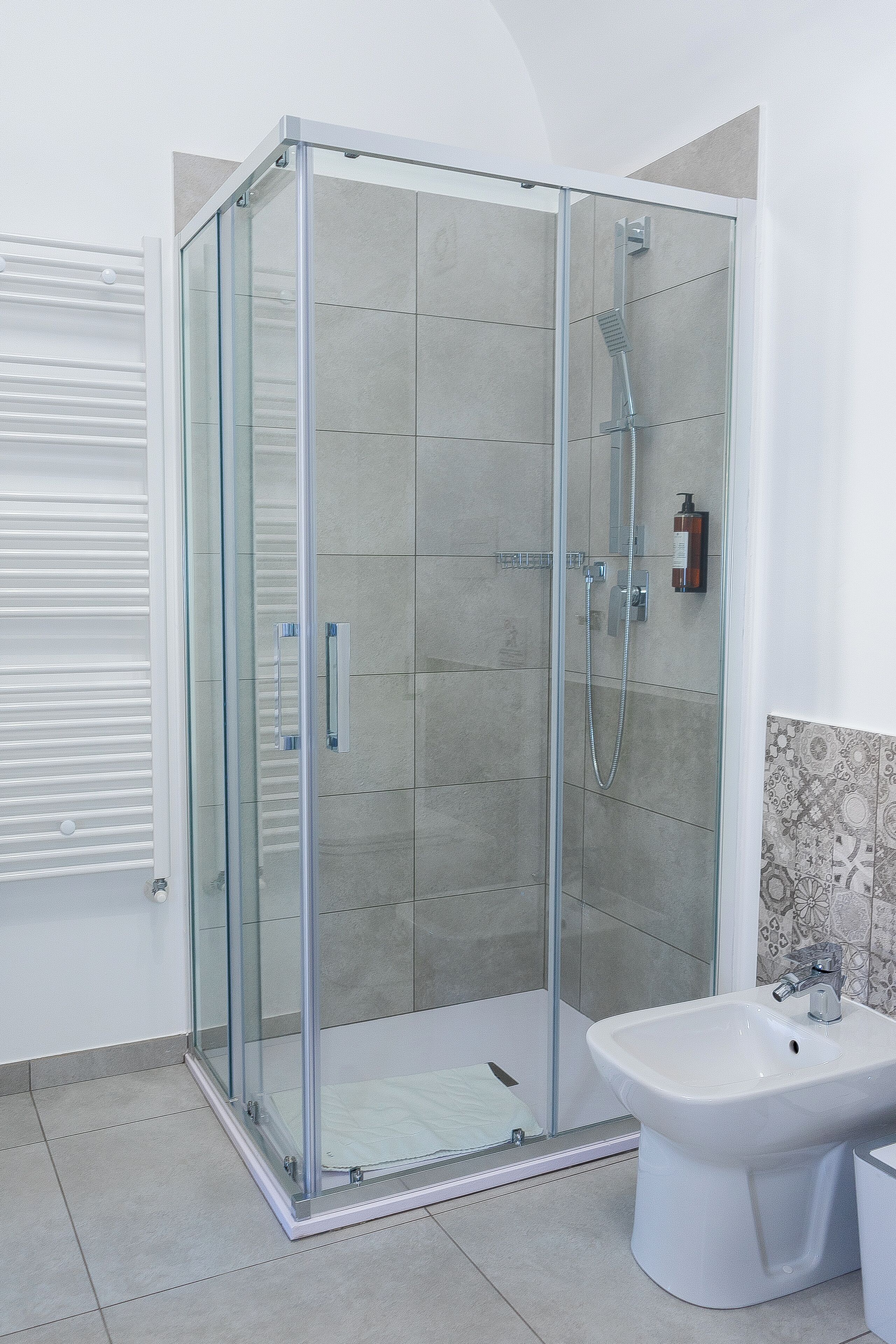 A modern bathroom with a glass-enclosed shower, a white sink, and a tiled floor.