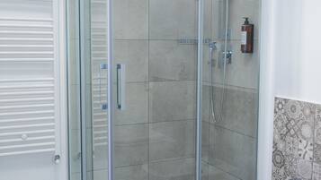 A modern bathroom with a glass-enclosed shower, a white sink, and a tiled floor.