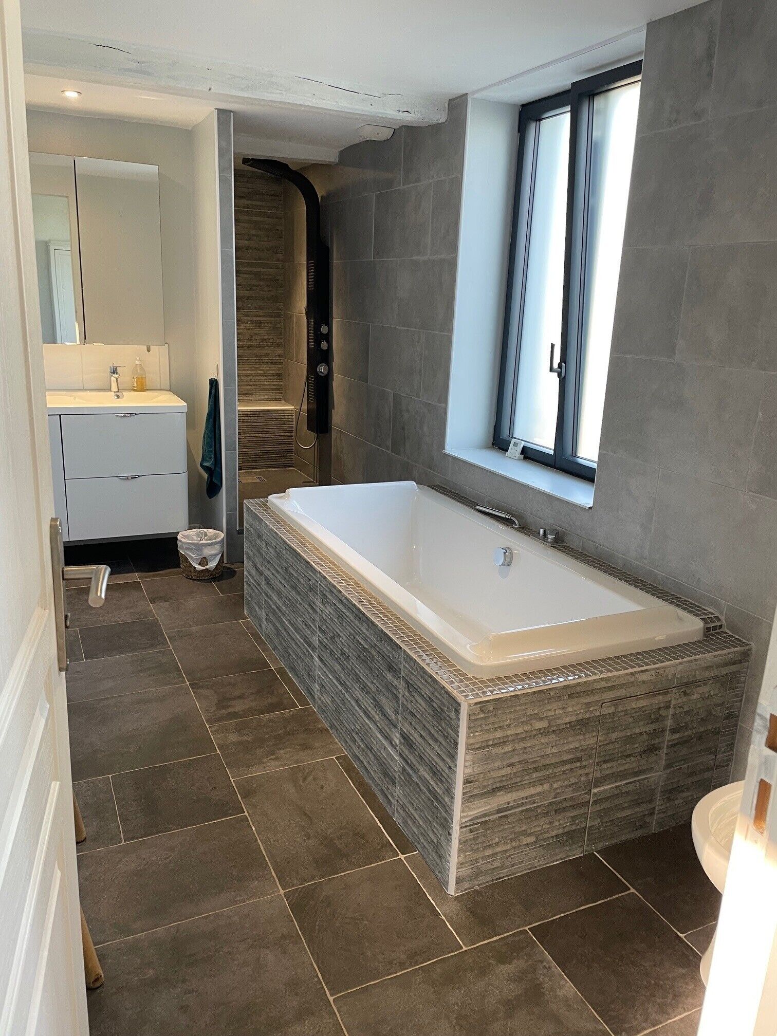 Ein modernes Badezimmer mit einer großen Badewanne, einer bodenebenen Dusche und einem Fenster für natürliches Licht.