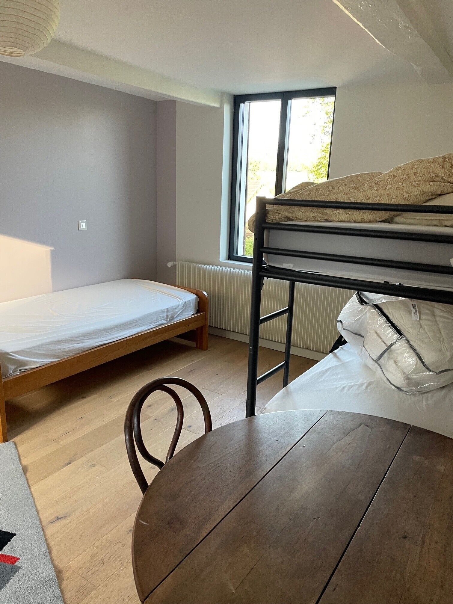 Een kleine, goed verlichte kamer met een stapelbed, een enkel bed en een ronde houten tafel.