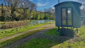 A small, rustic cabin by a river with a gravel path leading to it. - 1 Bed Cabin - Sleeps 2 - Hottub - Parking - Garden (Bideford)