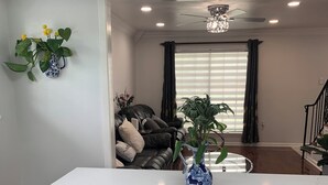 Un salon moderne avec un îlot central blanc, un ventilateur de plafond et une vue sur un canapé de couleur foncée et un escalier.