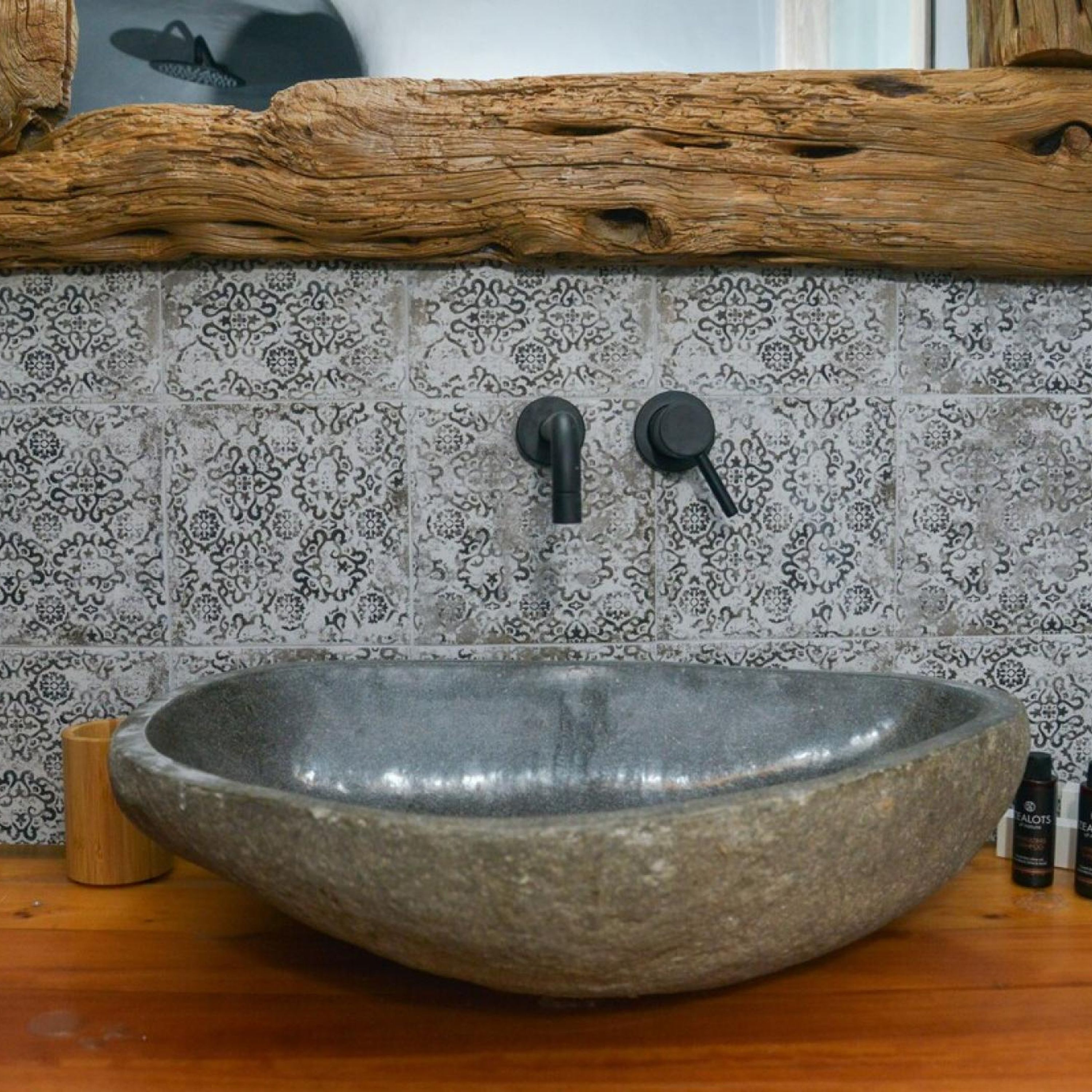 A stone sink with a modern faucet, set against a patterned tile backsplash.