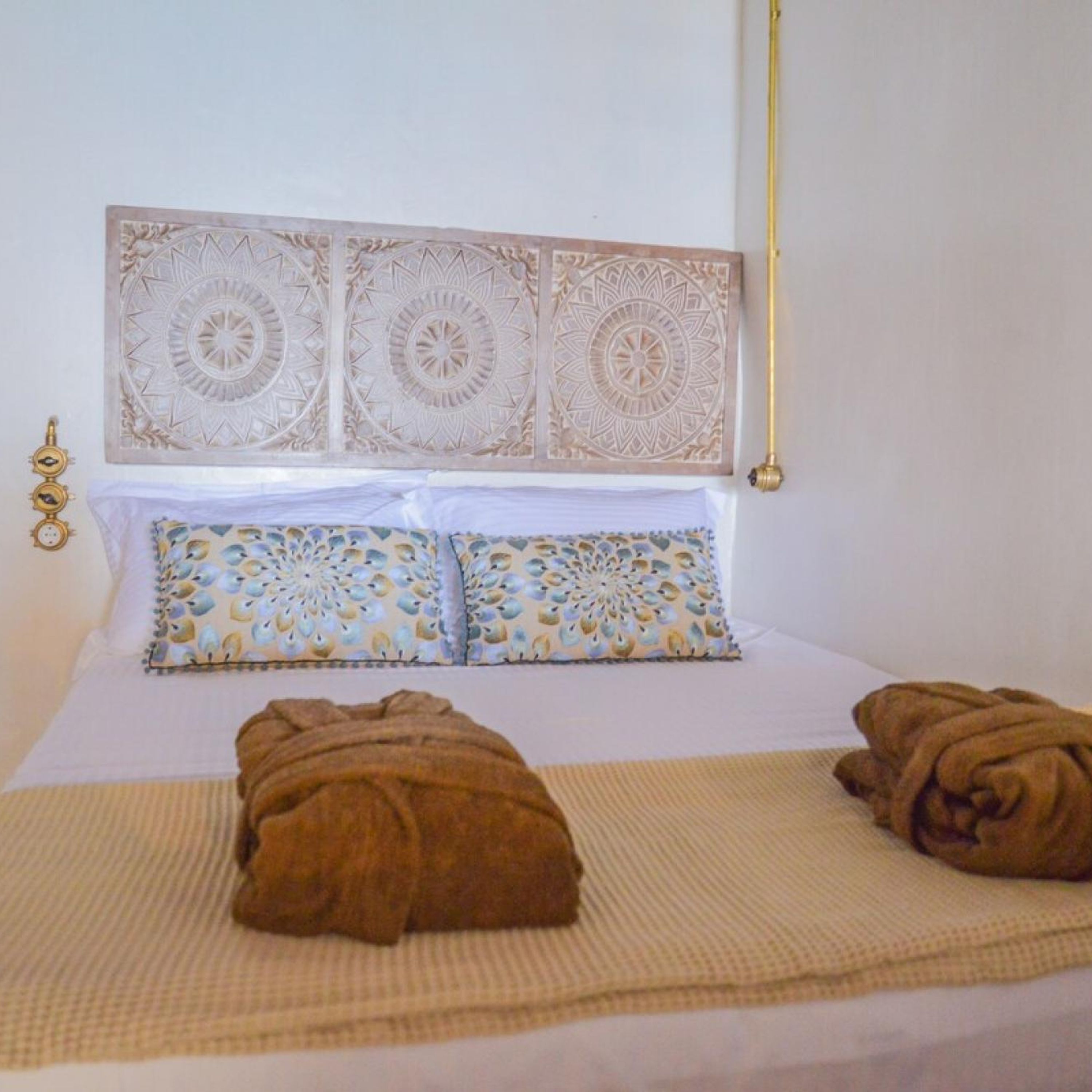 Una cama bien hecha con almohadas estampadas, un cabecero decorativo y dos toallas sobre la cama.