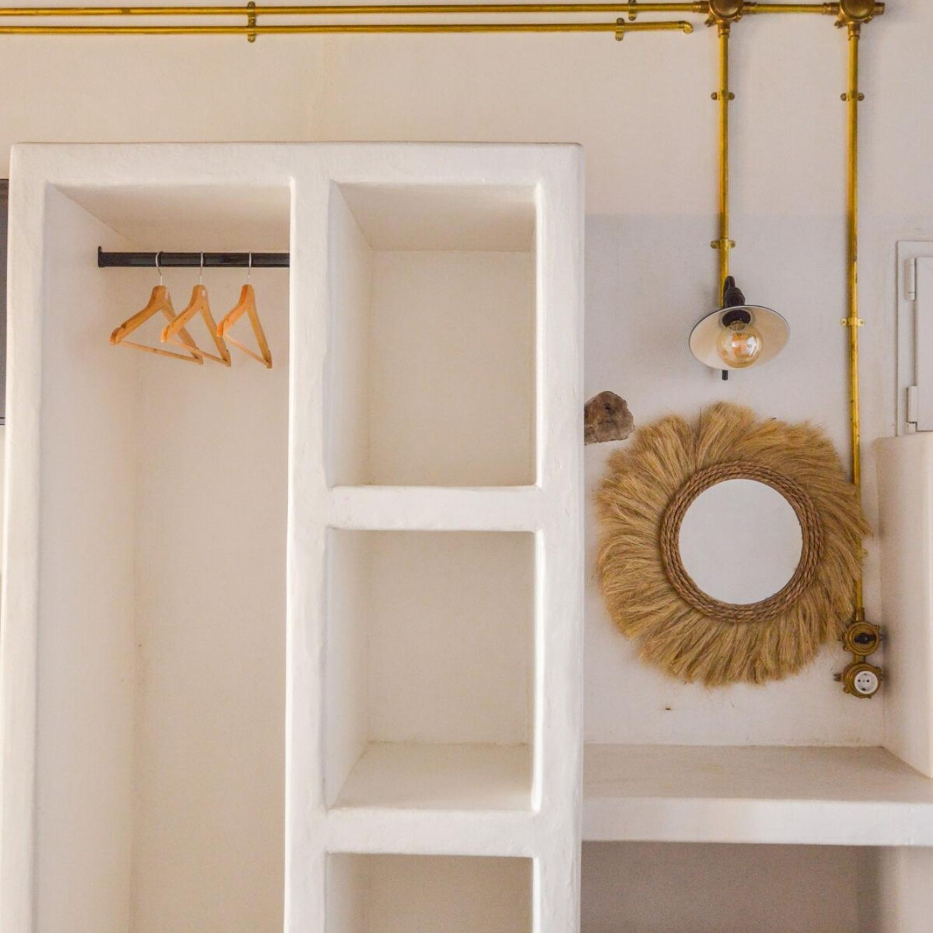 Een witte kast met open planken, een kledingroede en een wandlamp, plus een decoratieve spiegel.