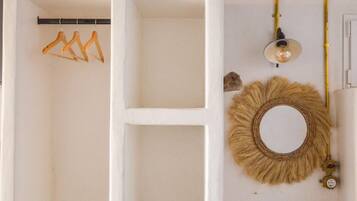 Een witte kast met open planken, een kledingroede en een wandlamp, plus een decoratieve spiegel.