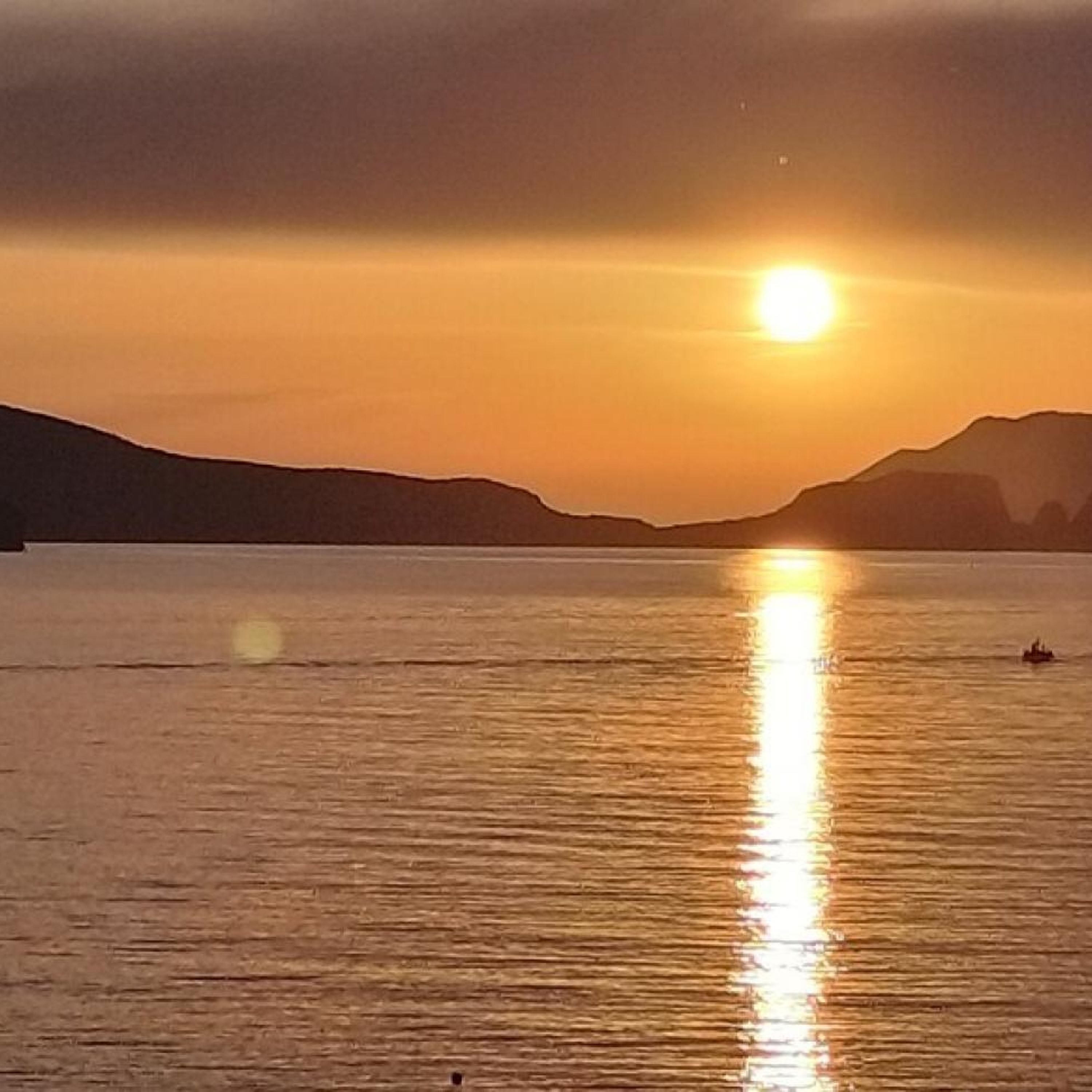 Un coucher de soleil sur une étendue d’eau calme, avec un bateau à l’horizon.