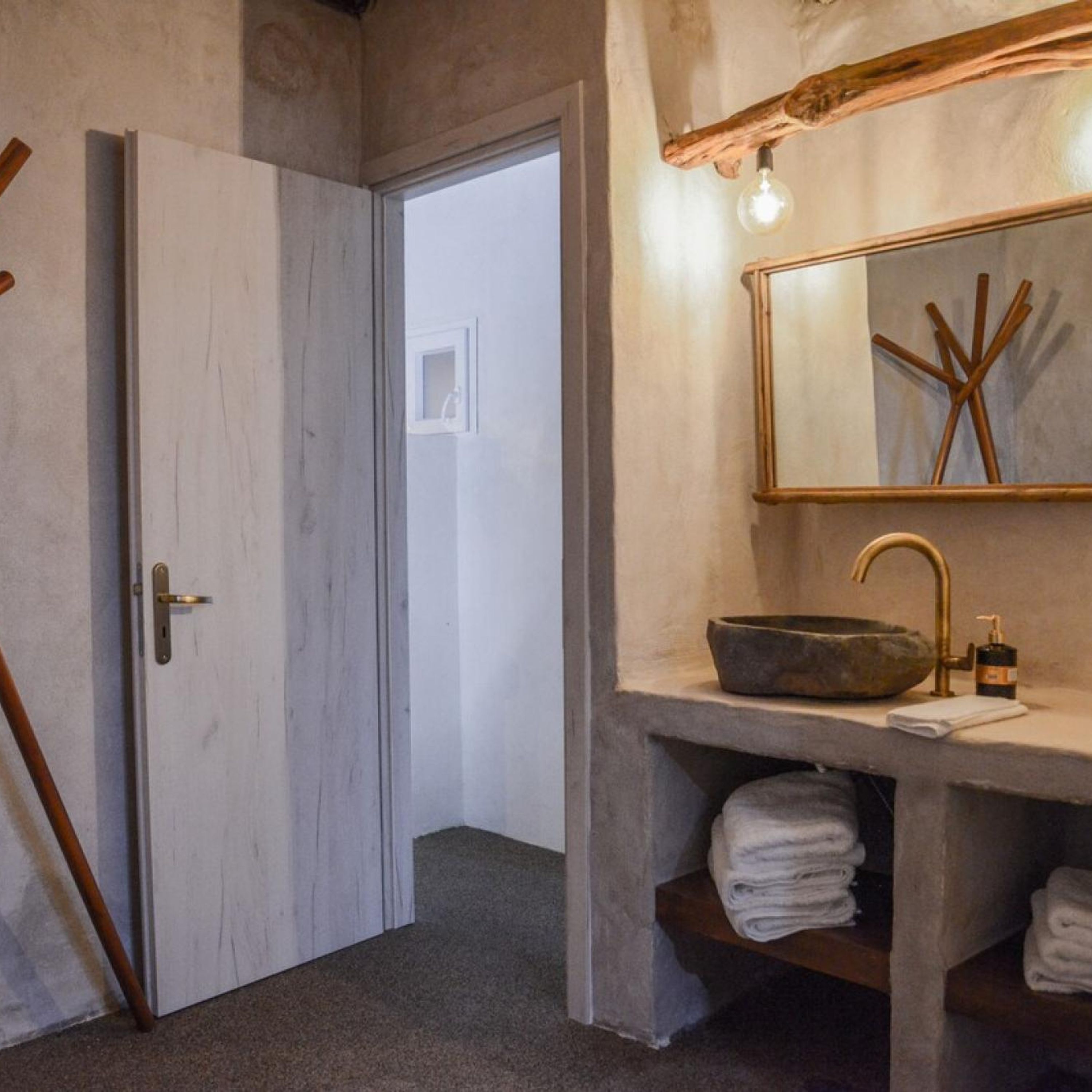 A bathroom with a stone sink, a wooden door, and a mirror with a light fixture.