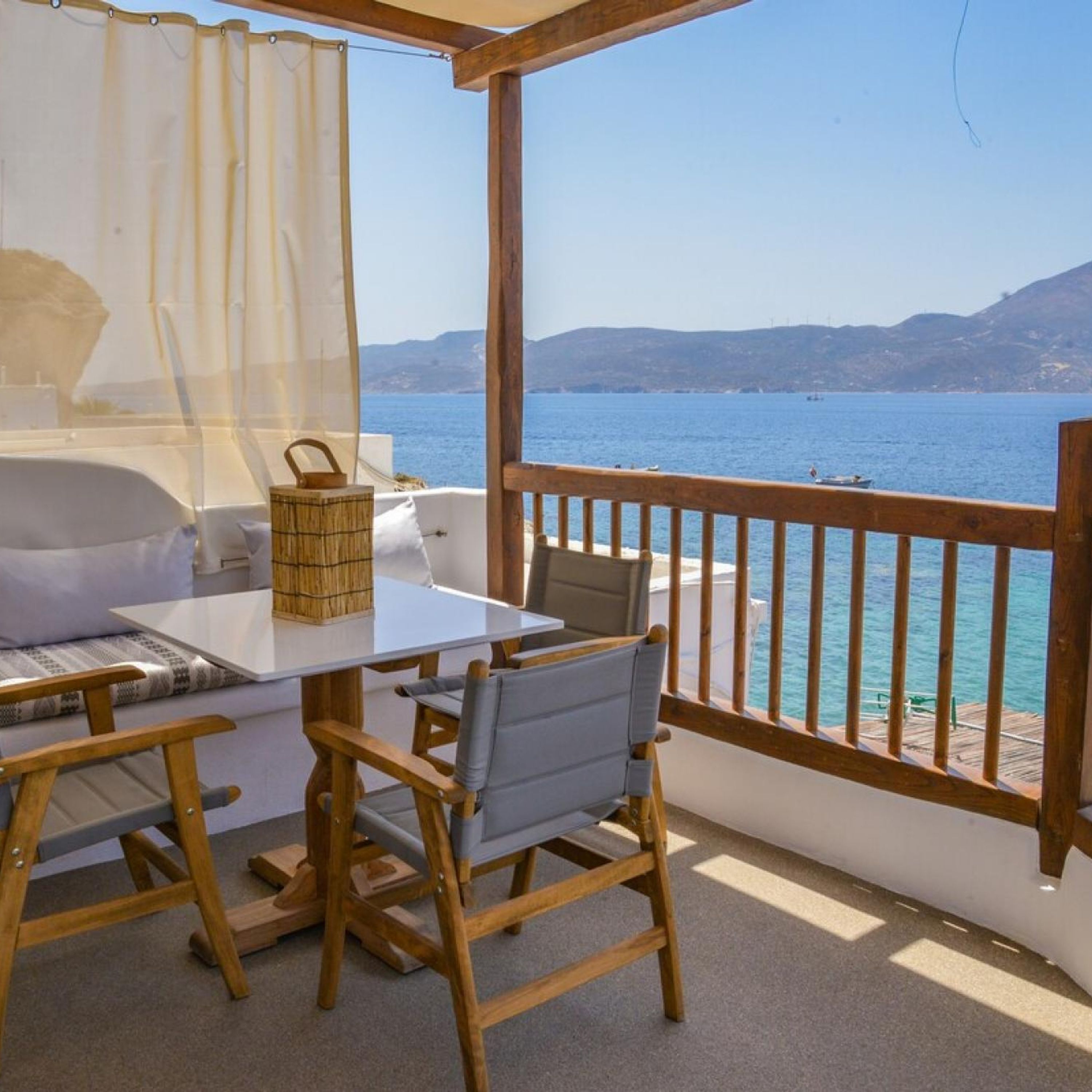 A balcony with a table and chairs, overlooking a body of water and distant hills.
