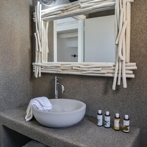 A bathroom with a white sink, a mirror with a natural wood frame, and three bottles of liquid on the counter. - Honeymoon Klima Suite (Milos)