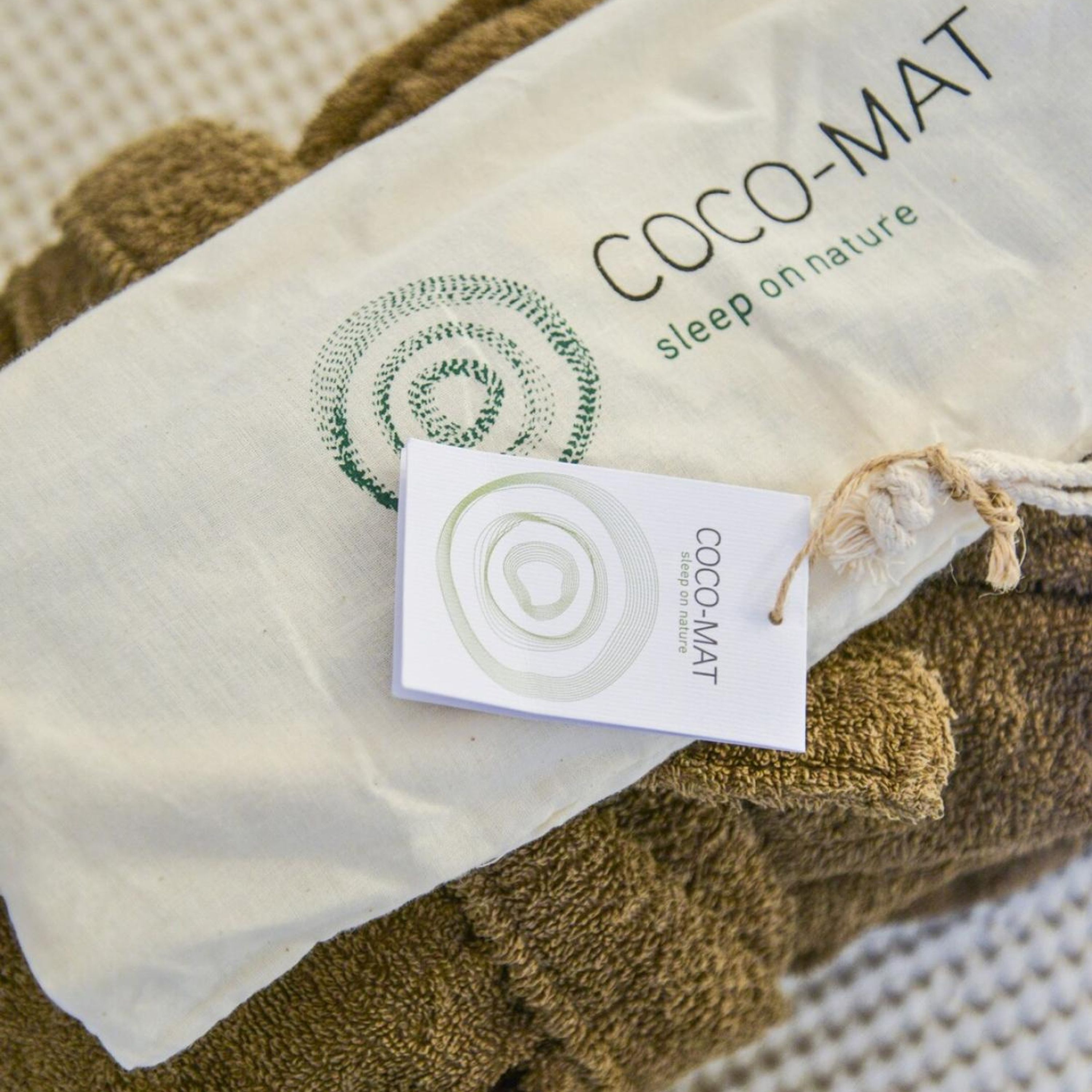 A white bag with a green circular logo and the text "COCO-MAT sleep on nature" on it.