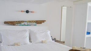 Habitación de hotel con una cama grande, ropa de cama blanca, cabecera de madera con ilustración de un barco, mesita de noche con lámpara y espejo en la pared.