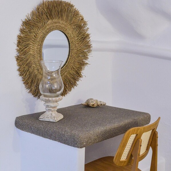 Una mesa de piedra con un espejo tejido y un florero de vidrio transparente.