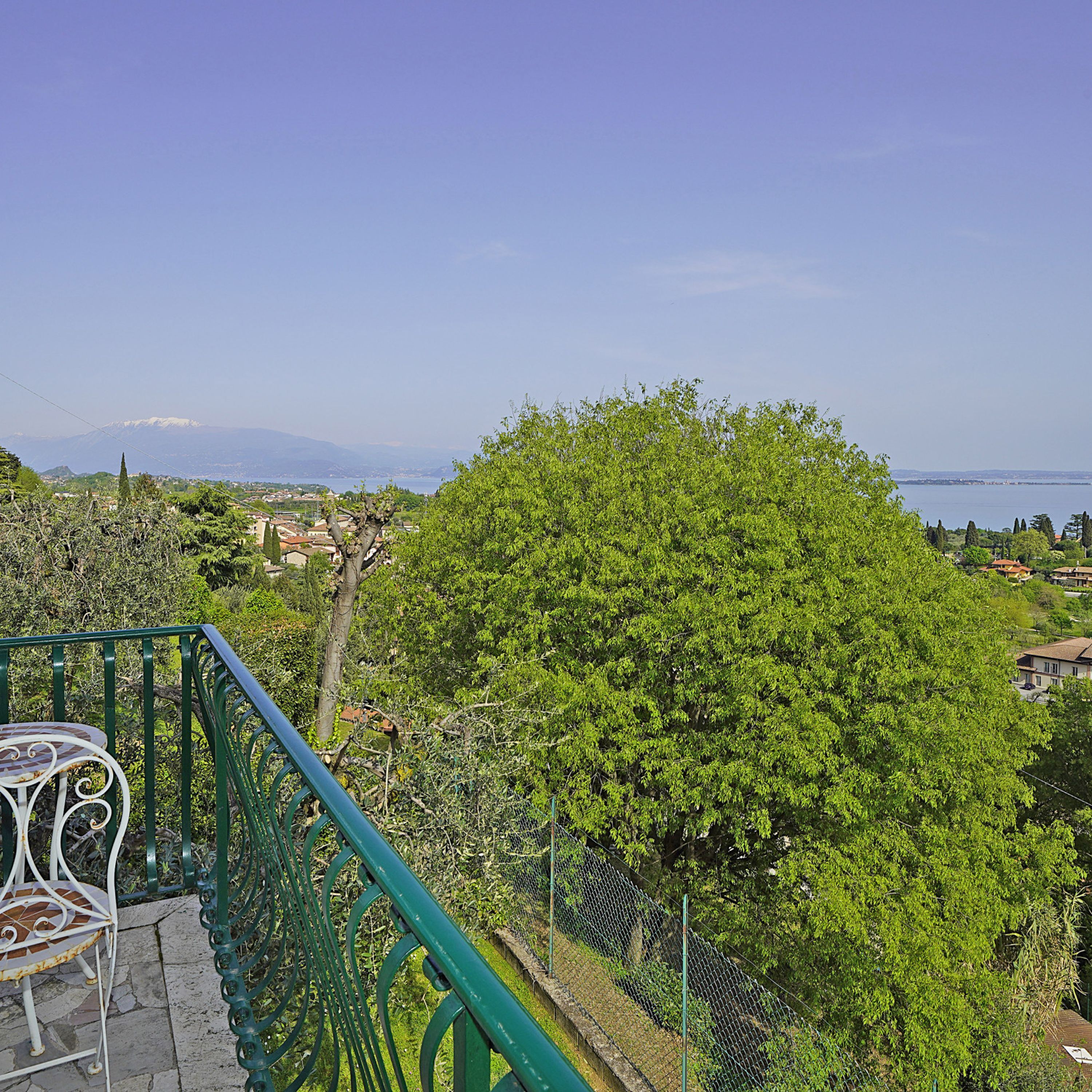 A balcony with a view of a tree, a fence, and a distant mountain range.