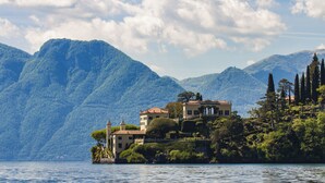 A lakeside property with a large house surrounded by lush greenery and mountains in the background.