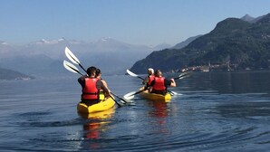 Two kayakers in yellow kayaks on a calm lake with mountains in the background.