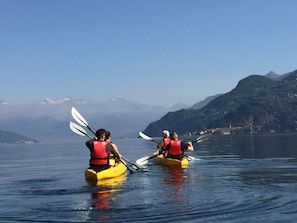Dos kayakistas en kayaks amarillos sobre un lago tranquilo, con montañas al fondo.