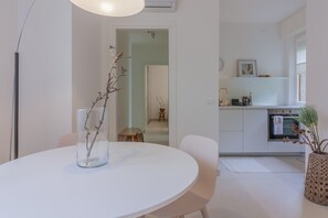 A modern kitchen with white cabinetry, a dining area with a round table, and a vase with branches.