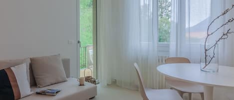 Una sala moderna con un sofá, una mesa de comedor, sillas y vistas a zonas verdes a través de las ventanas.