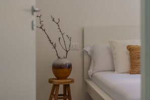 A bedroom with a bed, a bedside table with a vase, and a wall socket.