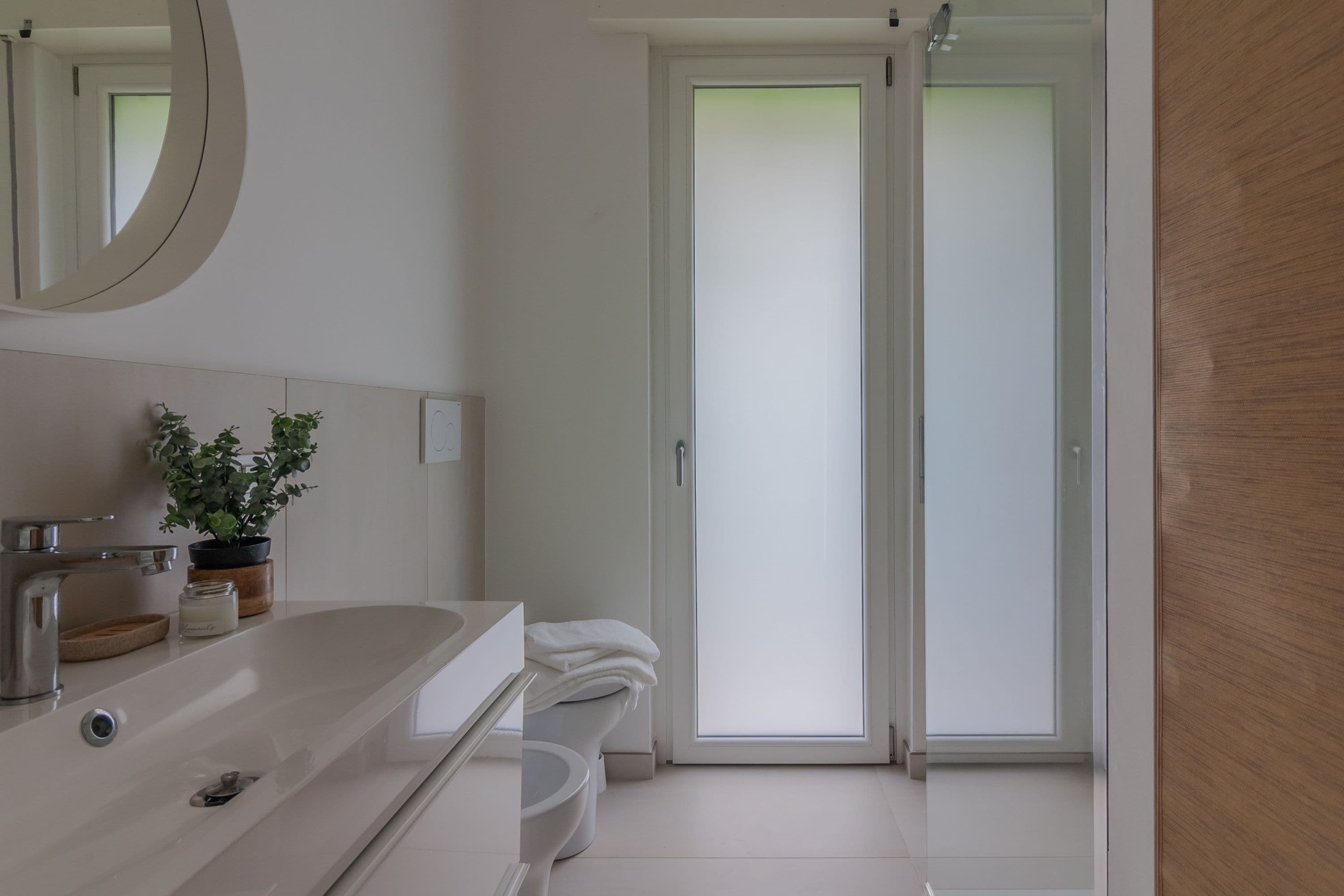 Een moderne badkamer met een wit wastafelmeubel, een spiegel, een potplant en een toilet.