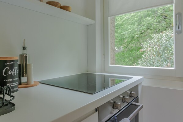 A kitchen with a modern design, featuring a glass countertop, a coffee machine, and a window with a view of greenery.