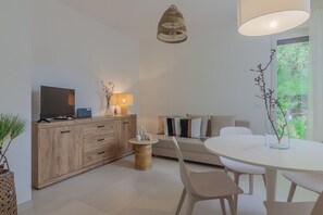 Una sala moderna con un mueble de madera, un televisor, una mesa redonda con sillas, un sofá y una lámpara colgante.