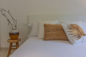A bed with white bedding, a wooden stool, and a vase with branches.