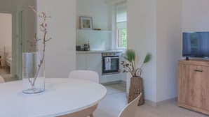 Une cuisine moderne avec des meubles blancs, un four encastré et un coin repas comprenant une table ronde et des chaises.