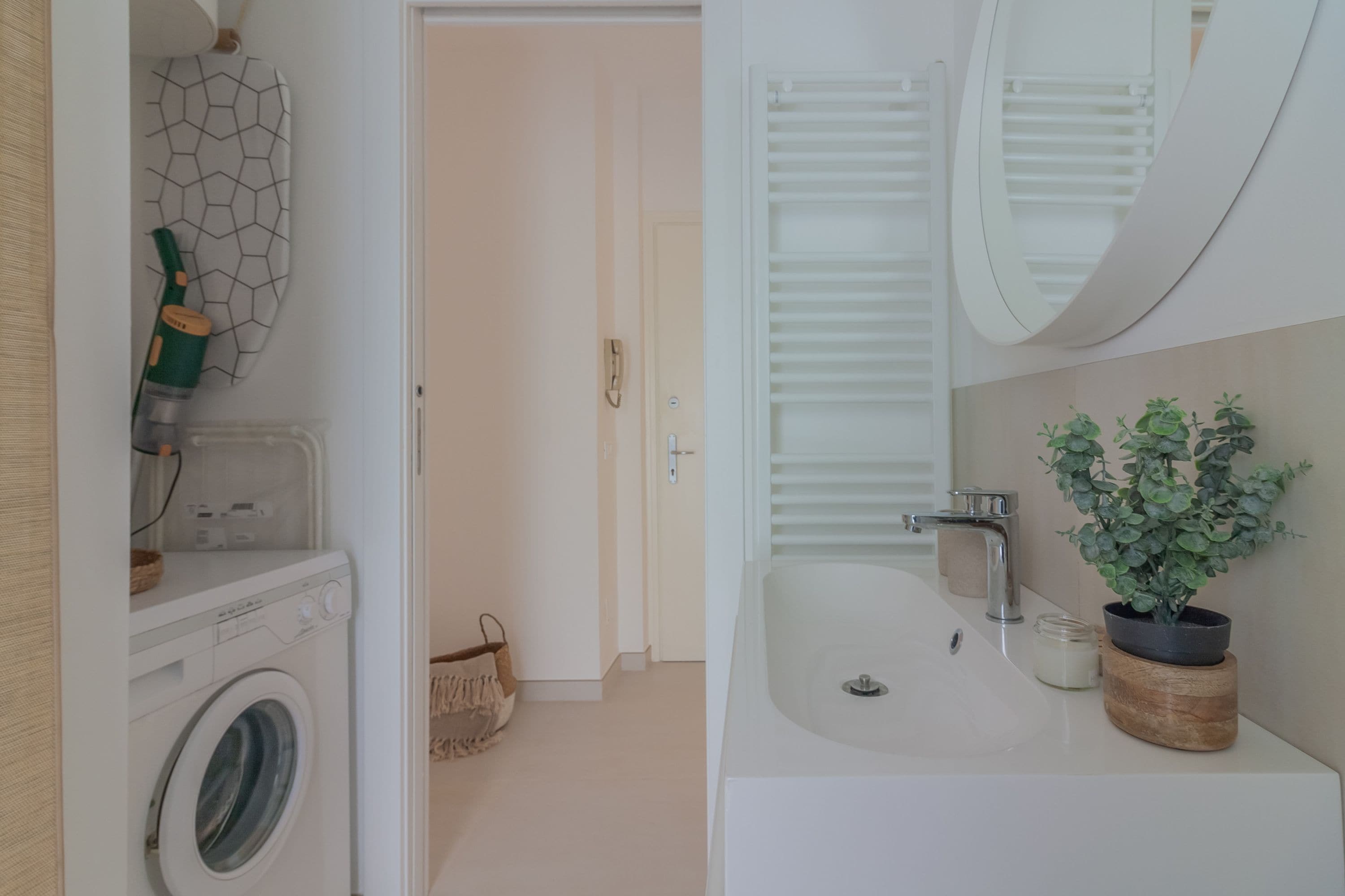 A modern bathroom with a washing machine, a sink, and a potted plant.
