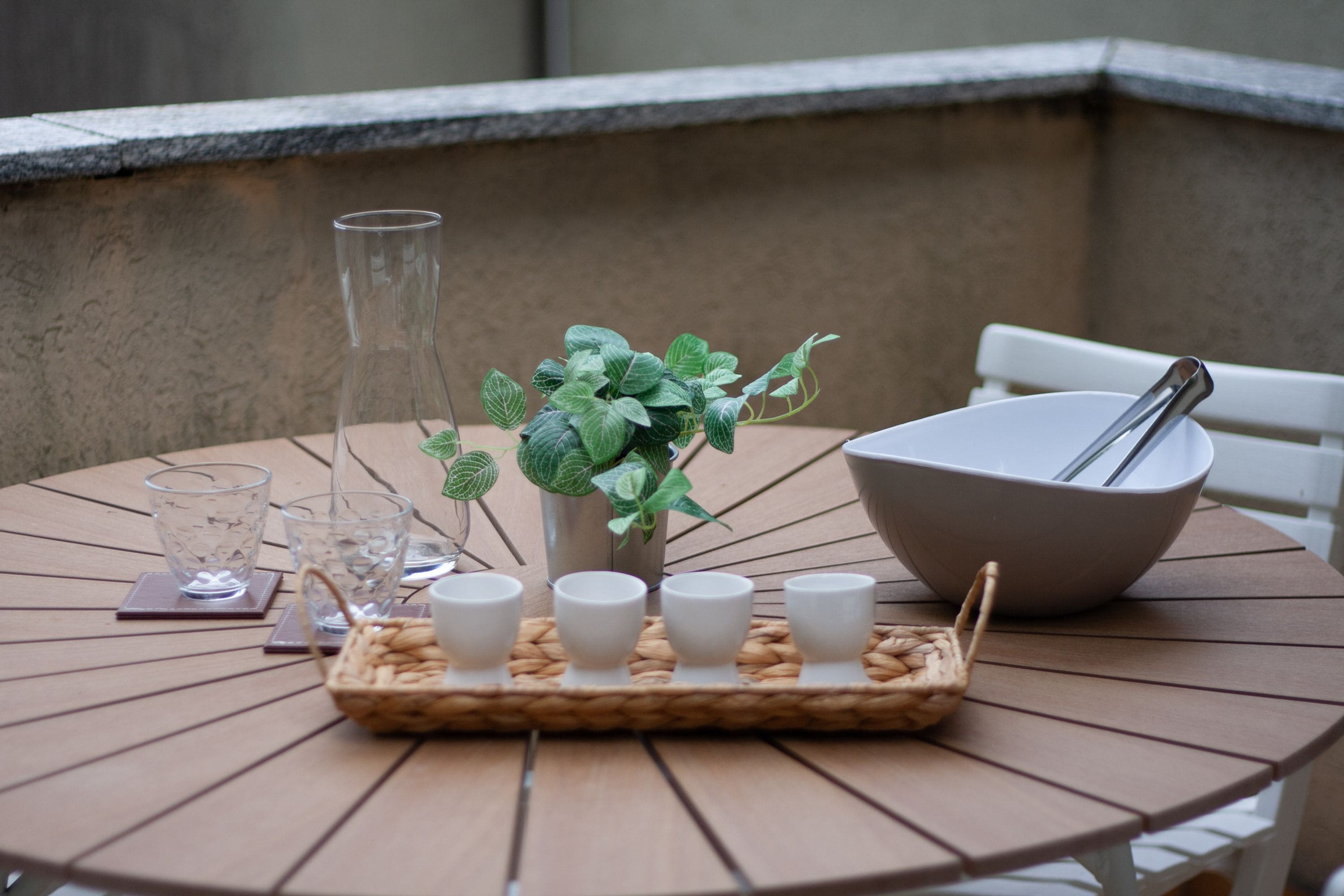 A round table with a glass pitcher, a bowl, and a tray with cups and a spoon.