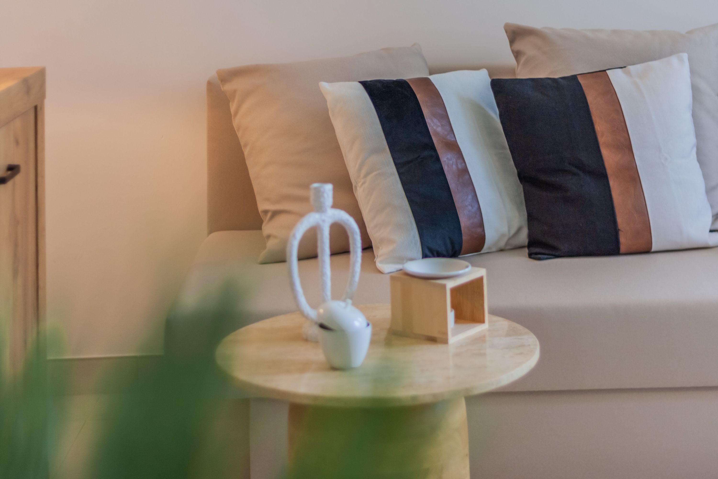 A modern living room with a sofa, pillows, a small table with a white object, and a wooden side table.