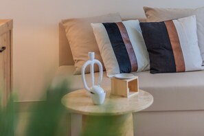 A modern living room with a sofa, pillows, a small table with a white object, and a wooden side table. - Profumo di Lago in Perledo (Perledo)